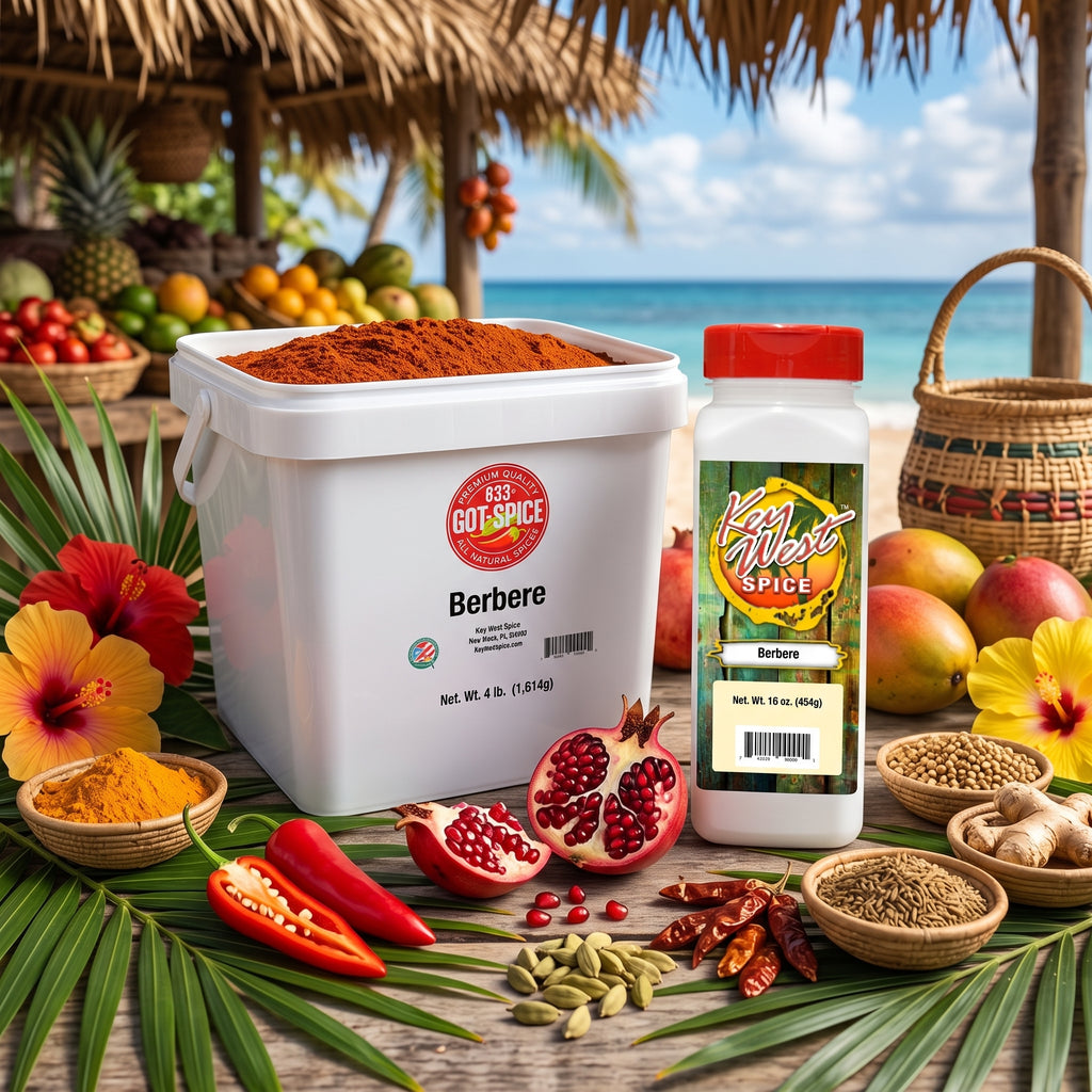 A large white tub of Goots Spice Berbere and a smaller bottle of the same spice are displayed on a tropical beach table with palm leaves, mangoes, pomegranates, chili peppers, and other spices. The background shows a beach and ocean under a thatched roof.