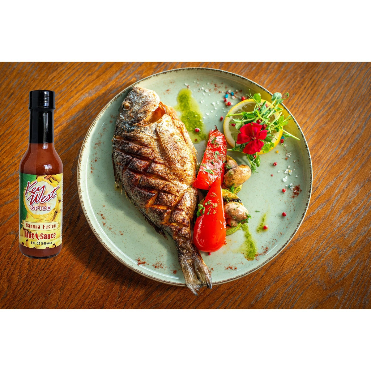 Key West Spice Banana Fusion Hot Sauce bottle with fish illustration, 5 oz., featuring vibrant tropical fruit and seafood-inspired design.