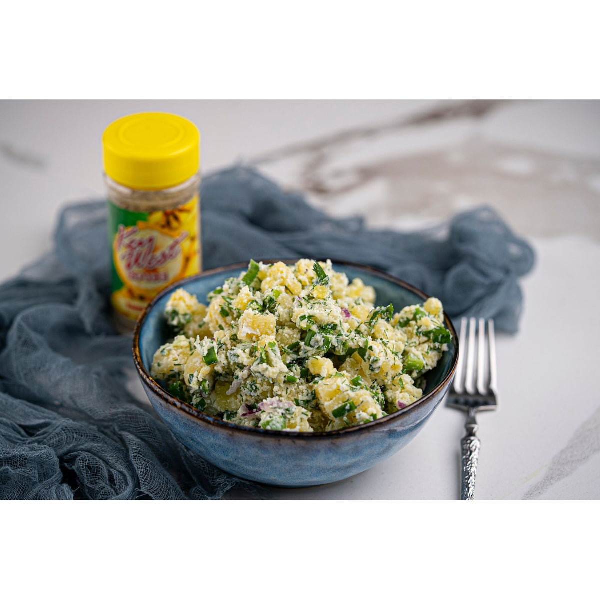 Banana Fusion salt-free, sugar-free spice blend from Key West Spice, shown in a jar alongside a potato salad dish.