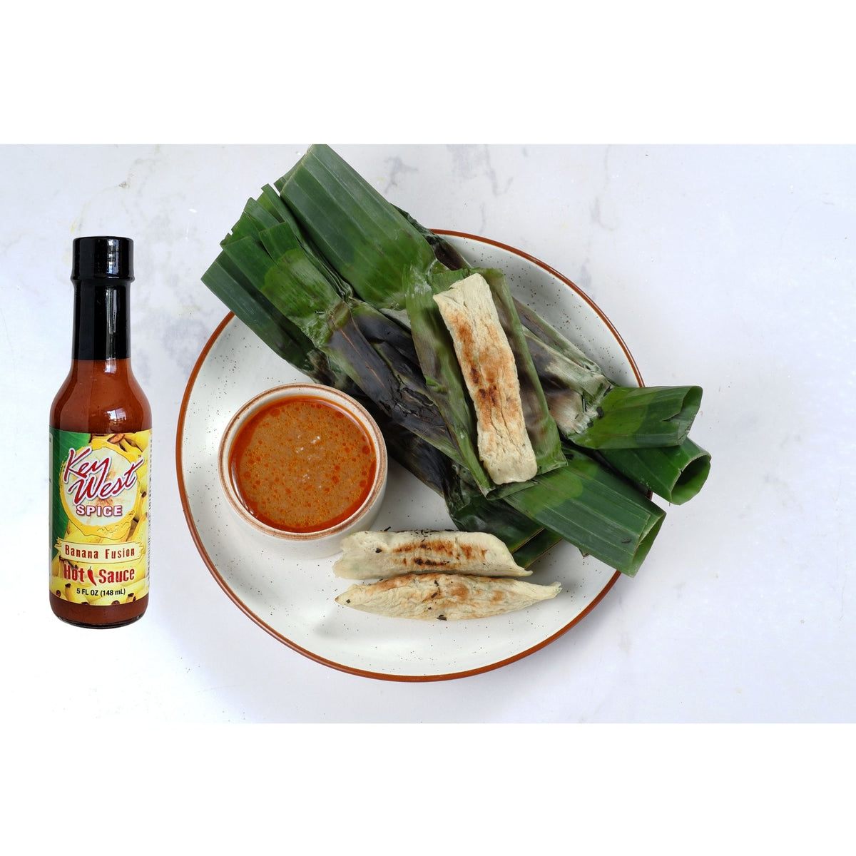 Key West Spice Fusion Hot Sauce Assortment of Four 5 oz bottles with banana and fish-themed labels, showcasing vibrant sauce colors and packaging.