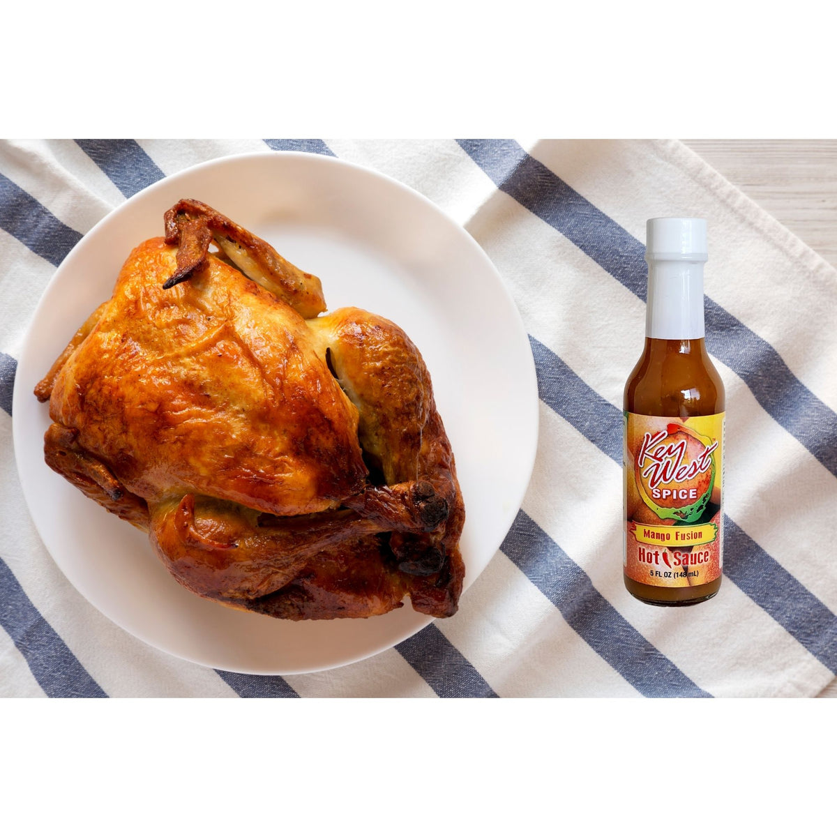 Key West Spice Mango Fusion Hot Sauce bottle next to grilled chicken, showcasing vibrant mango flavor and spicy sauce.