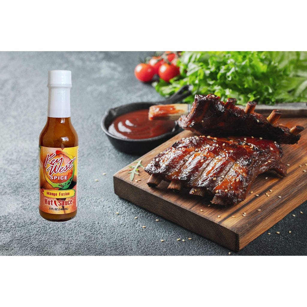 Key West Spice Mango Fusion Hot Sauce bottle on ribs, showcasing the flavorful fusion hot sauce for dishes and grilling.
