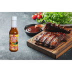 Key West Spice Mango Fusion Hot Sauce bottle on ribs, showcasing the flavorful fusion hot sauce for dishes and grilling.